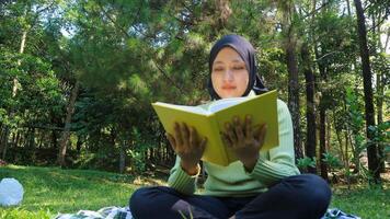 entspannt Muslim Frau genießen Wochenende beim Park, Sitzung auf Gras und lesen Buch, leeren Raum foto