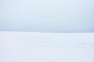 weiche minimalistische Landschaft des Schneefeldes mit Schneemobilspuren. foto