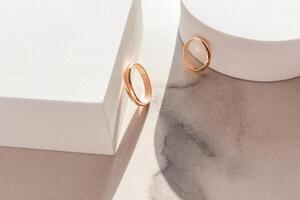 Hochzeit Anordnung von zwei Gold Hochzeit Ringe auf ein Weiß Marmor Hintergrund unter geometrisch Podien. Hochzeit Layout Konzept. foto