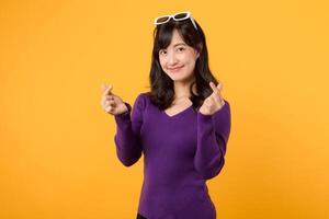 Mini Herz Zeichen Geste. jung 30er Jahre asiatisch Frau tragen lila Hemd tun Mini Herz Hand Geste mit glücklich zuversichtlich Lächeln isoliert auf Gelb Hintergrund. Liebe Herz Hand Geste Konzept. foto