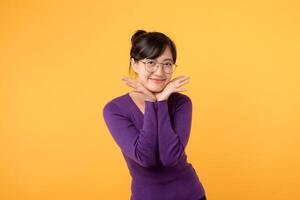 Porträt von glücklich asiatisch Frau 30er Jahre tragen lila Sweatshirt Hemd lächelnd, posieren süß ziemlich Geste Stehen gegen Gelb Studio Hintergrund. foto
