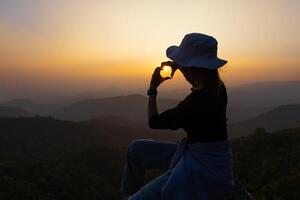 Silhouette von Frau Herstellung ein Herz gestalten mit ihr Hände im Vorderseite von ein Sonnenuntergang. Symbol von Liebe. Manifestation von Liebe. Ausdruck von Gefühle. Glück, Jugend. foto