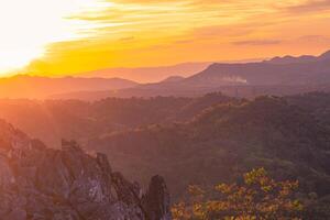 das atemberaubend Aussicht von ein Touristen Standpunkt wie Sie gehen Nieder ein Hügel auf ein nebelig Weg mit ein Hügel und ein Hintergrund von ein golden Himmel im Wald Park, Thailand. Vogel Auge Sicht. Antenne Sicht. Regenwald foto