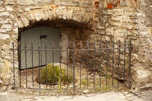 ein Geheimnis Passage im das Backstein Mauer hinter ein gesperrt grau Metall Tor und ein gesperrt bearbeitet Eisen Pforte. ein Beton Halbkreis mit Grün Moos verhindert Passage zu das Eingang. horizontal. foto