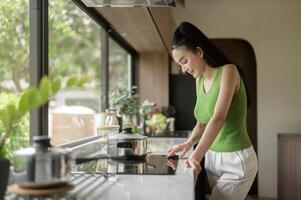 asiatisch Frau Kochen und riechen Verkostung Suppe im ein Topf im das Küche Tabelle beim heim. foto