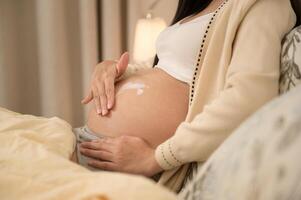 schön schwanger Frau bewirbt sich feuchtigkeitsspendend, strecken Kennzeichen Sahne auf Bauch, Fruchtbarkeit Unfruchtbarkeit Behandlung, In-vitro-Fertilisation, Zukunft Mutterschaft Konzept foto