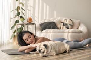 asiatisch Frau im Sportbekleidung ausüben und tun Yoga mit süß Hund im Leben Zimmer beim heim, gesund Lebensstil, mental Gesundheit Konzept. foto