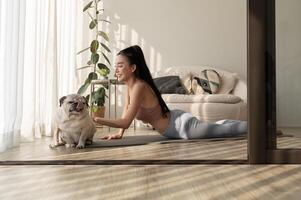 asiatisch Frau im Sportbekleidung ausüben und tun Yoga mit süß Hund im Leben Zimmer beim heim, gesund Lebensstil, mental Gesundheit Konzept. foto