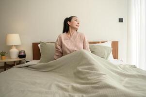 jung asiatisch Frau Dehnen im Bett nach aufwachen oben im das Morgen foto