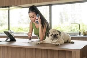 jung asiatisch Frau Arbeiten mit Tablette und genießen mit ihr Hund im das Küche beim Zuhause foto