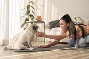 asiatisch Frau im Sportbekleidung ausüben und tun Yoga mit süß Hund im Leben Zimmer beim heim, gesund Lebensstil, mental Gesundheit Konzept. foto