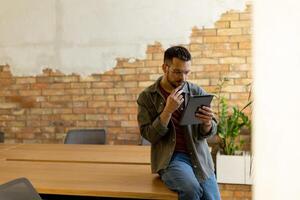 lächelnd Mann mit Tablette im ein modern gemauert Büro foto