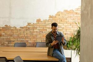 lächelnd Mann mit Tablette im ein modern gemauert Büro foto