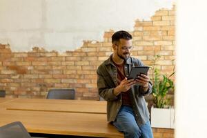 lächelnd Mann mit Tablette im ein modern gemauert Büro foto