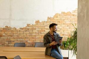lächelnd Mann mit Tablette im ein modern gemauert Büro foto
