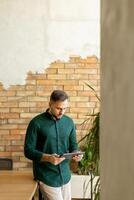 lächelnd Mann mit Tablette im ein modern gemauert Büro foto