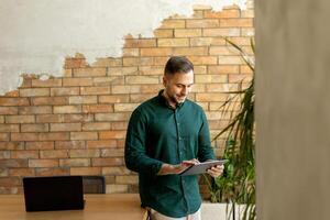 lächelnd Mann mit Tablette im ein modern gemauert Büro foto