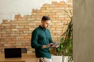 lächelnd Mann mit Tablette im ein modern gemauert Büro foto