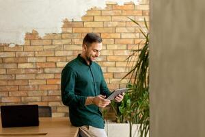 lächelnd Mann mit Tablette im ein modern gemauert Büro foto