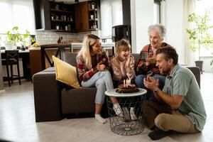 freudig Familie feiern Großmütter Geburtstag mit Kuchen im ein gemütlich Leben Zimmer foto