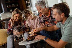 freudig Familie feiern Großmütter Geburtstag mit Kuchen im ein gemütlich Leben Zimmer foto