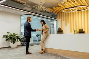 warm Handschlag zwischen Kollegen im modern Büro Empfangshalle unter Umgebungs Beleuchtung foto