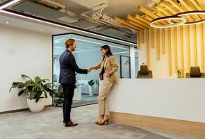 warm Handschlag zwischen Kollegen im modern Büro Empfangshalle unter Umgebungs Beleuchtung foto