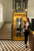 Geschäftsfrau verlassen Aufzug im modern Büro Empfangshalle während ein Telefon Konversation foto