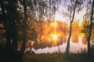 Dämmerung auf ein See oder Fluss mit ein Himmel reflektiert im das Wasser, Birke Bäume auf das Ufer und das Sonnenstrahlen brechen durch Sie und Nebel im Herbst. Ästhetik von Jahrgang Film. foto