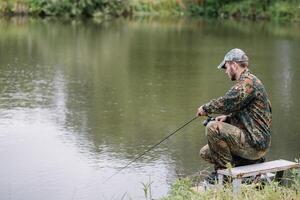 Fischer auf das Sommer- Hintergrund. Fischer im seine Hand halten Spinnen. Angeln, Spinnen Spule, Fisch, breg Flüsse. - - das Konzept von ein ländlich Flucht. Artikel Über Angeln. foto