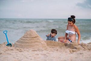 Mutter und Sohn spielen auf das Strand beim das Sonnenuntergang Zeit. Konzept von freundlich Familie foto