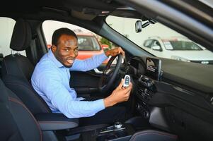 glücklich Auto Käufer, Neu Auto Inhaber Konzept. Porträt von aufgeregt jung afrikanisch amerikanisch Kerl im Händler Ausstellungsraum foto