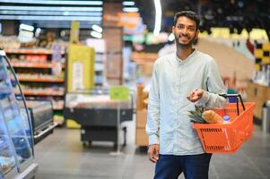 Porträt von glücklich indisch Mann Stehen im Vorderseite von das Produkt Zähler im ein Lebensmittelgeschäft speichern. Mann Kauf Lebensmittelgeschäft zum Zuhause im Supermarkt. foto