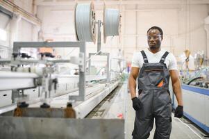 afrikanisch männlich Ingenieur. Steuerung ein Material Produktion Maschine System, Arbeiten im ein Plastik und Stahl Industrie hinsichtlich das Firma Produkt Geschäft. foto