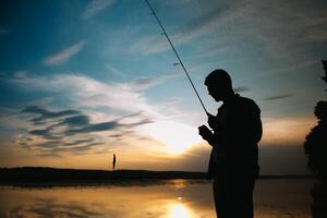 Fischer beim Sonnenuntergang auf das Fluss .Schön Sommer- Landschaft mit Sonnenuntergang auf das Fluss. Angeln. Spinnen beim Sonnenuntergang. Silhouette von ein Fischer. foto