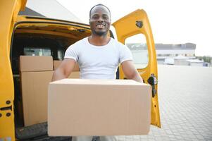 afrikanisch männlich Post- Lieferung Kurier Mann im Vorderseite von Auto liefern Paket foto