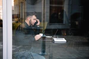 jung Geschäftsmann reden auf Handy, Mobiltelefon Telefon während Arbeiten auf Laptop im Cafe foto