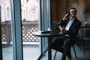 jung Geschäftsmann reden auf Handy, Mobiltelefon Telefon während Arbeiten auf Tablette im Cafe. foto