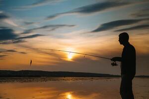 ein Fischer Silhouette Angeln beim Sonnenuntergang. frisches Wasser Angeln, Fang von Fisch. foto