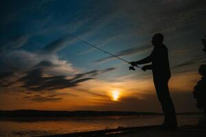 Fischer beim Sonnenuntergang auf das Fluss .Schön Sommer- Landschaft mit Sonnenuntergang auf das Fluss. Angeln. Spinnen beim Sonnenuntergang. Silhouette von ein Fischer. foto