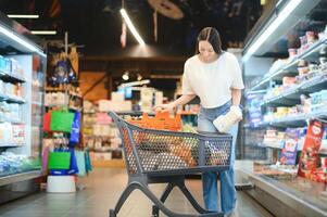 Lebensmittel Einkaufen. Porträt von lächelnd glücklich Frau gelehnt auf Wagen Wagen im Supermarkt foto