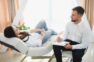 Psychologe nehmen Anmerkungen während Therapie Session mit traurig jung Frau im seine Büro. Kopieren Raum foto