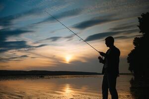 Angeln. Spinnen beim Sonnenuntergang. Silhouette von ein Fischer foto