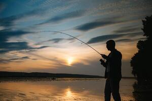 Fischer beim Sonnenuntergang auf das Fluss .Schön Sommer- Landschaft mit Sonnenuntergang auf das Fluss. Angeln. Spinnen beim Sonnenuntergang. Silhouette von ein Fischer. foto