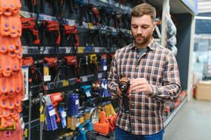 hübscher junger Mann, der Werkzeuge im Baumarkt einkauft foto