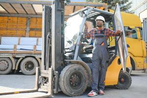 Porträt von ein glücklich afrikanisch amerikanisch männlich Arbeiter Fahren Gabelstapler beim Arbeitsplatz foto