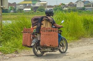 ein Paket Kurier ist Senden Pakete oder Ladung mit ein Motorrad Über beschädigt Straßen, Indonesien, 16 Januar 2024. foto