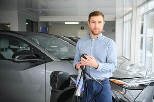 ein glücklich Mann wählt ein Neu elektrisch Auto beim ein Auto Händler. das Konzept von Kauf ein ökologisch Auto foto