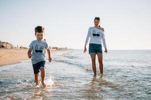 Mutter und Sohn spielen auf das Strand beim das Sonnenuntergang Zeit. Konzept von freundlich Familie foto