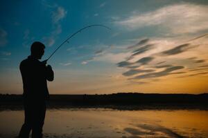 Angeln. Spinnen beim Sonnenuntergang. Silhouette von ein Fischer. foto